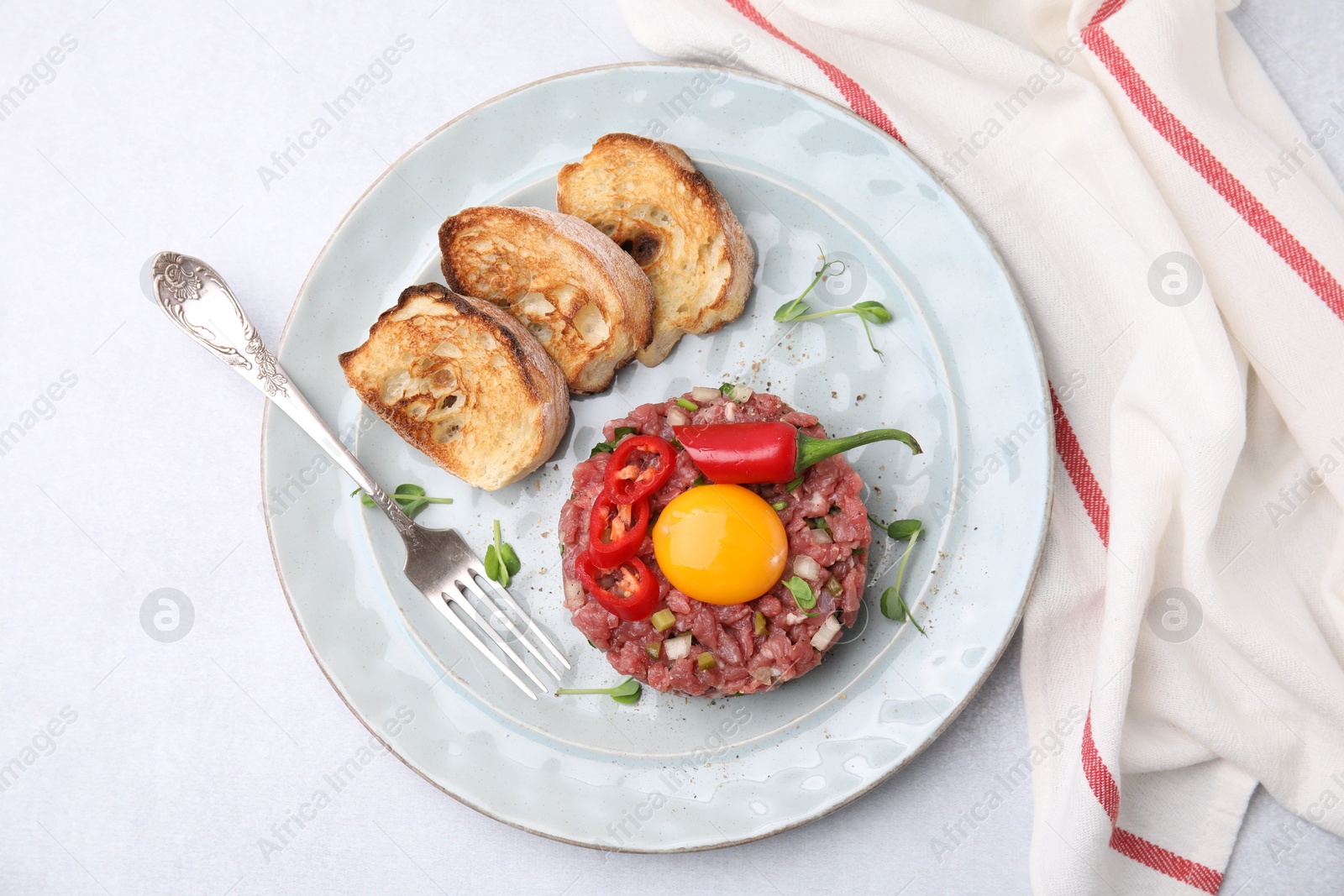 Photo of Tasty beef steak tartare served with yolk, toasted bread and other accompaniments on white table, top view