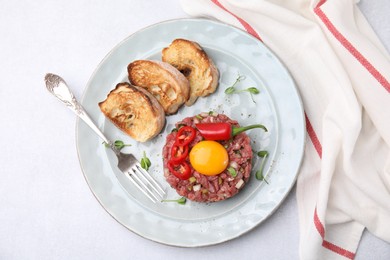 Photo of Tasty beef steak tartare served with yolk, toasted bread and other accompaniments on white table, top view