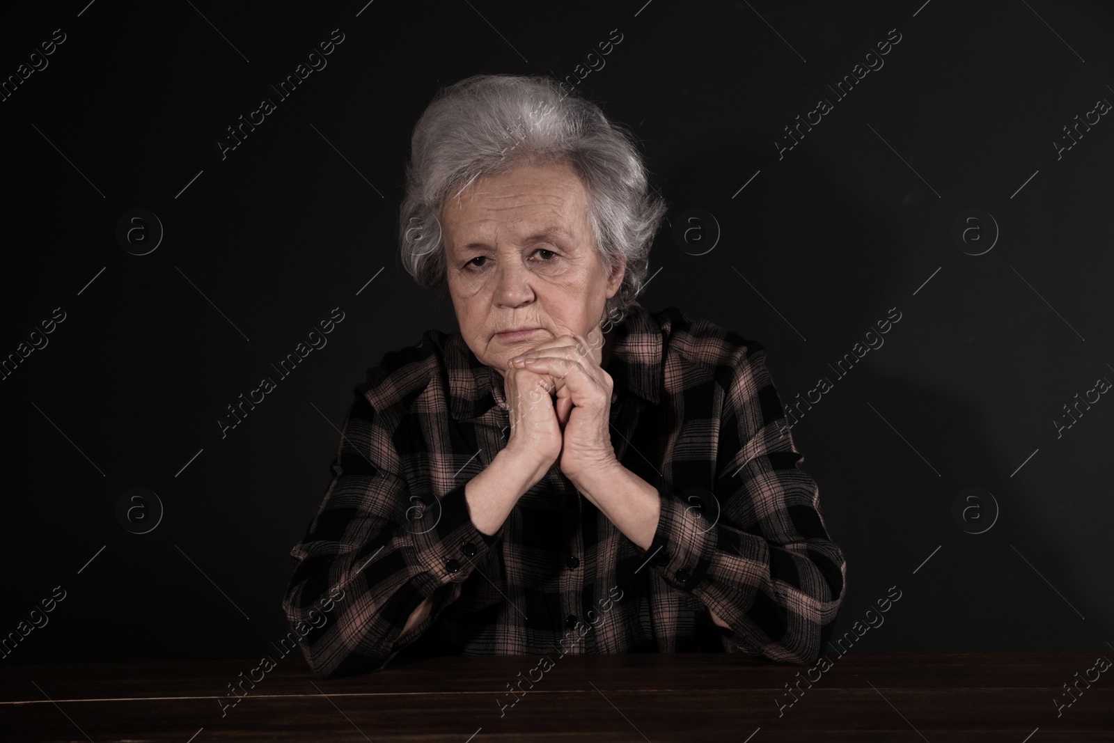 Photo of Poor upset woman sitting at table on dark background