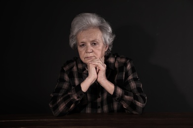 Photo of Poor upset woman sitting at table on dark background