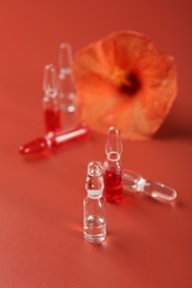 Photo of Skincare ampoules and hibiscus flower on coral background