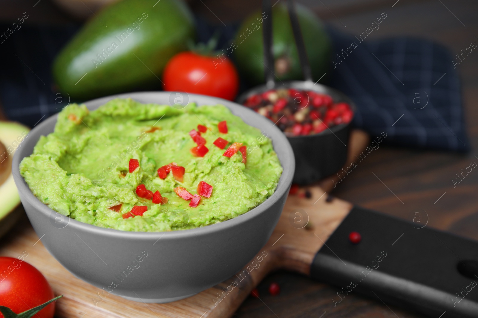 Photo of Bowl of delicious guacamole and ingredients on wooden table, closeup. Space for text