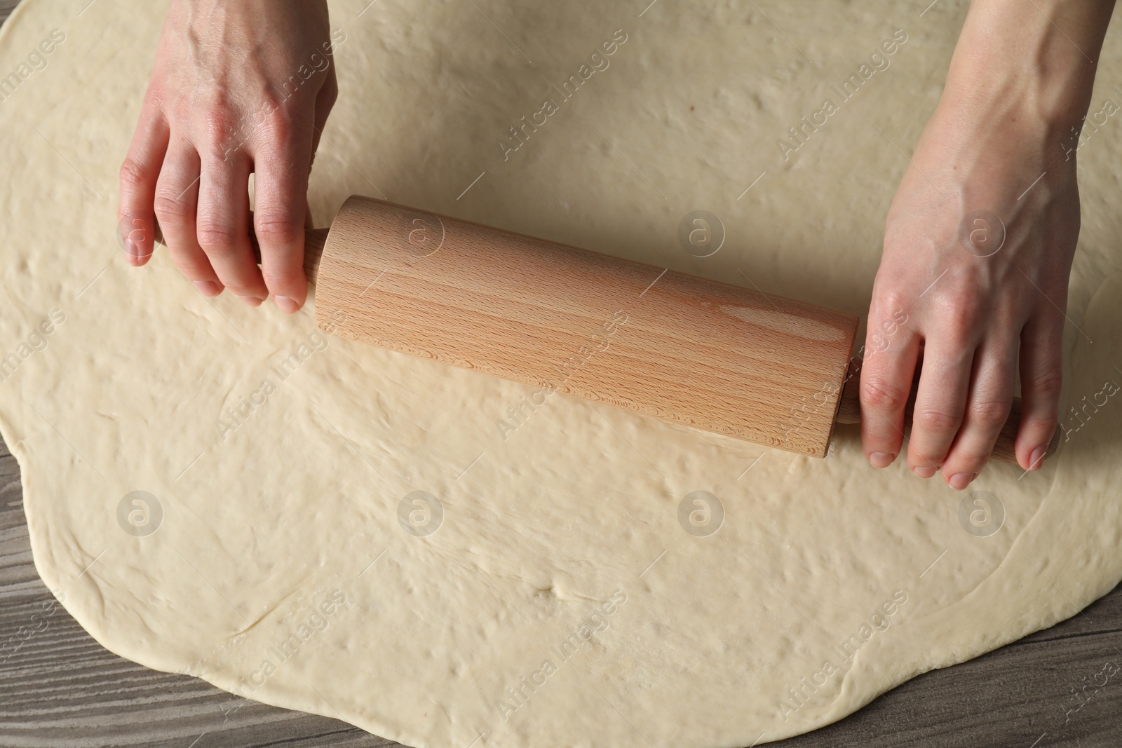 Photo of Woman rolling raw dough at wooden table, closeup