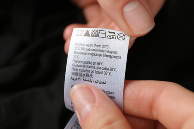 Photo of Woman reading clothing label with care symbols on black shirt, closeup