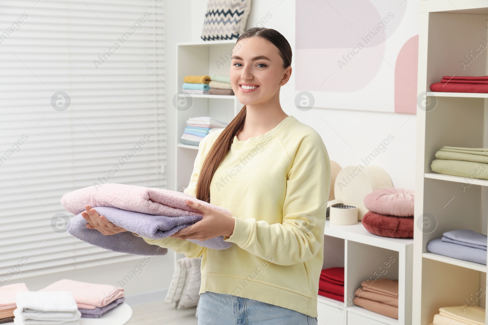 Photo of Smiling young woman holding new towels in home textiles store