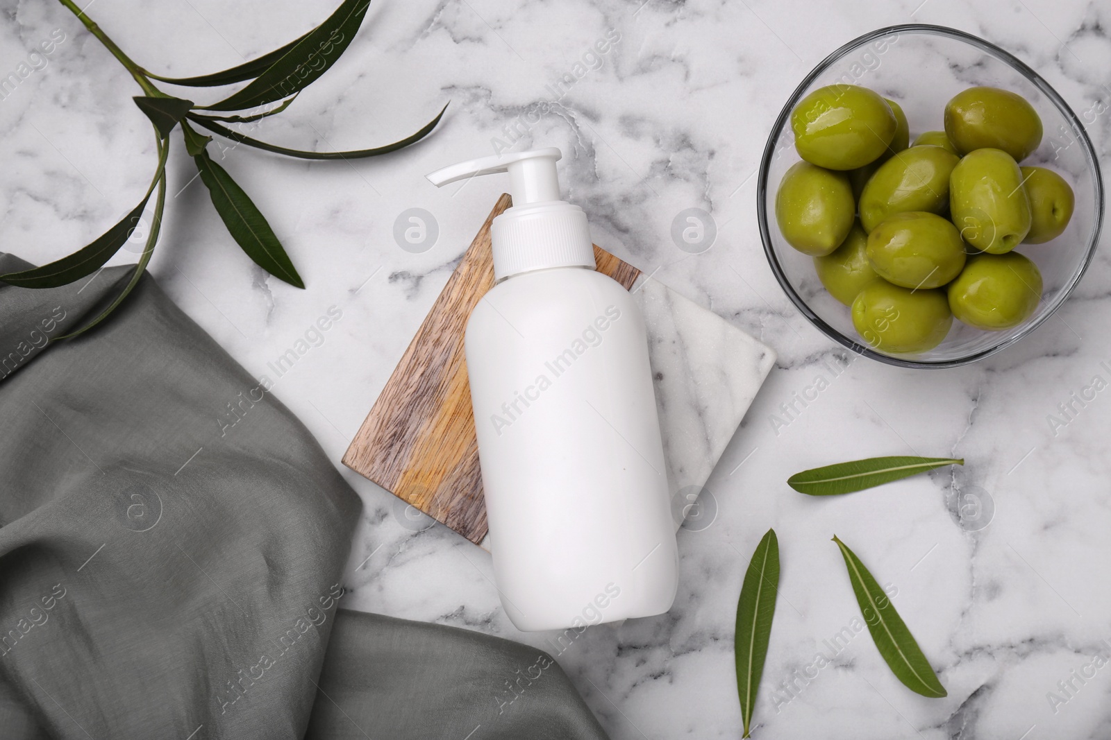 Photo of Bottle of cosmetic product with olive essential oil and leaves on white marble table, flat lay