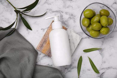 Photo of Bottle of cosmetic product with olive essential oil and leaves on white marble table, flat lay