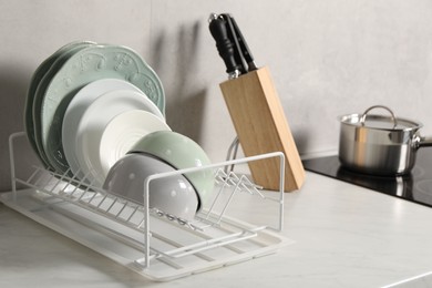 Drainer with different clean dishware on white table indoors