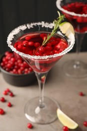 Photo of Tasty cranberry cocktail with rosemary and lime in glasses on grey table against black background, closeup