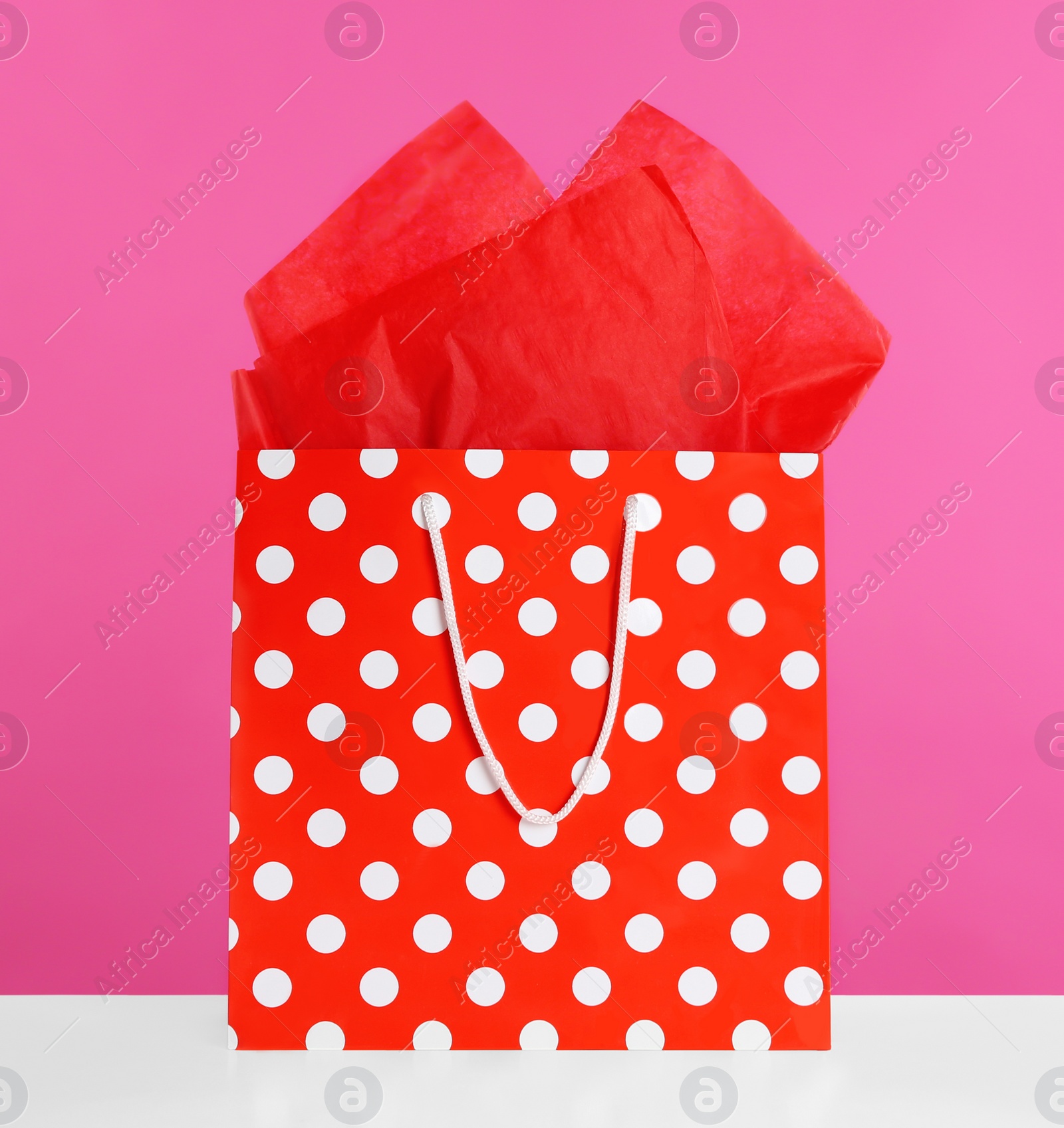 Photo of Gift bag with paper on white table against pink background