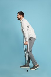 Full length portrait of man with crutches on light blue background