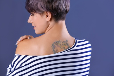 Trendy young woman with tattoo on color background