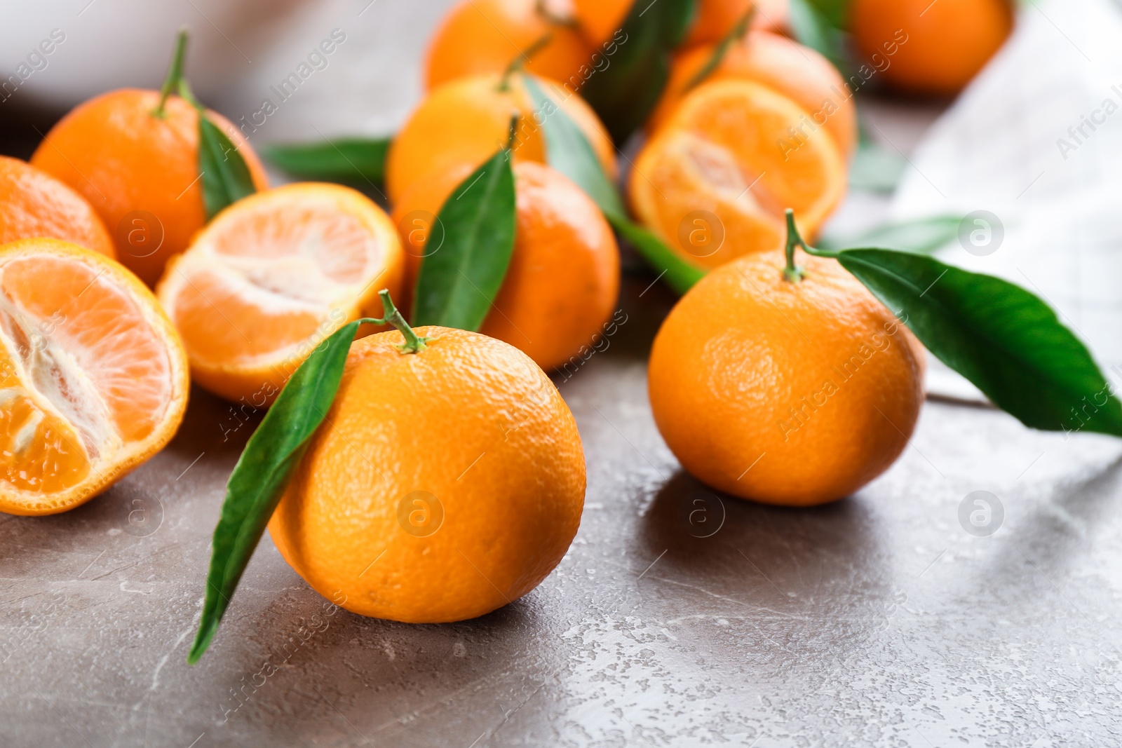 Photo of Fresh tangerines with green leaves on grey table, closeup