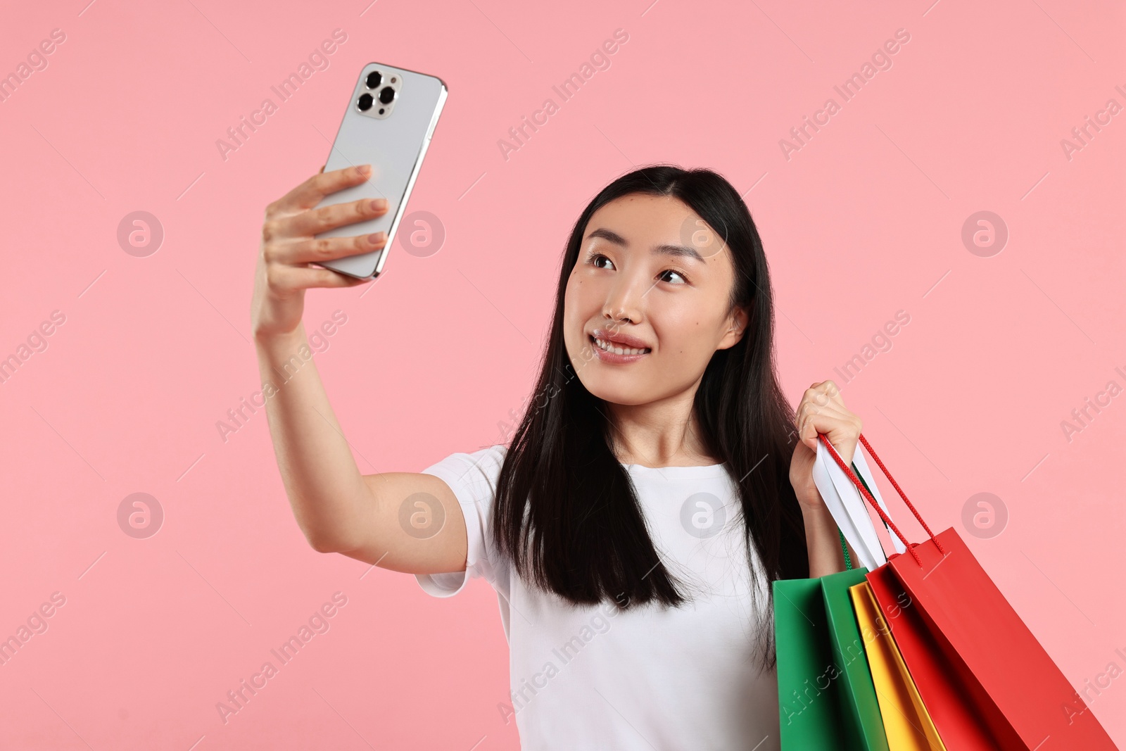 Photo of Smiling woman with shopping bags taking selfie on pink background