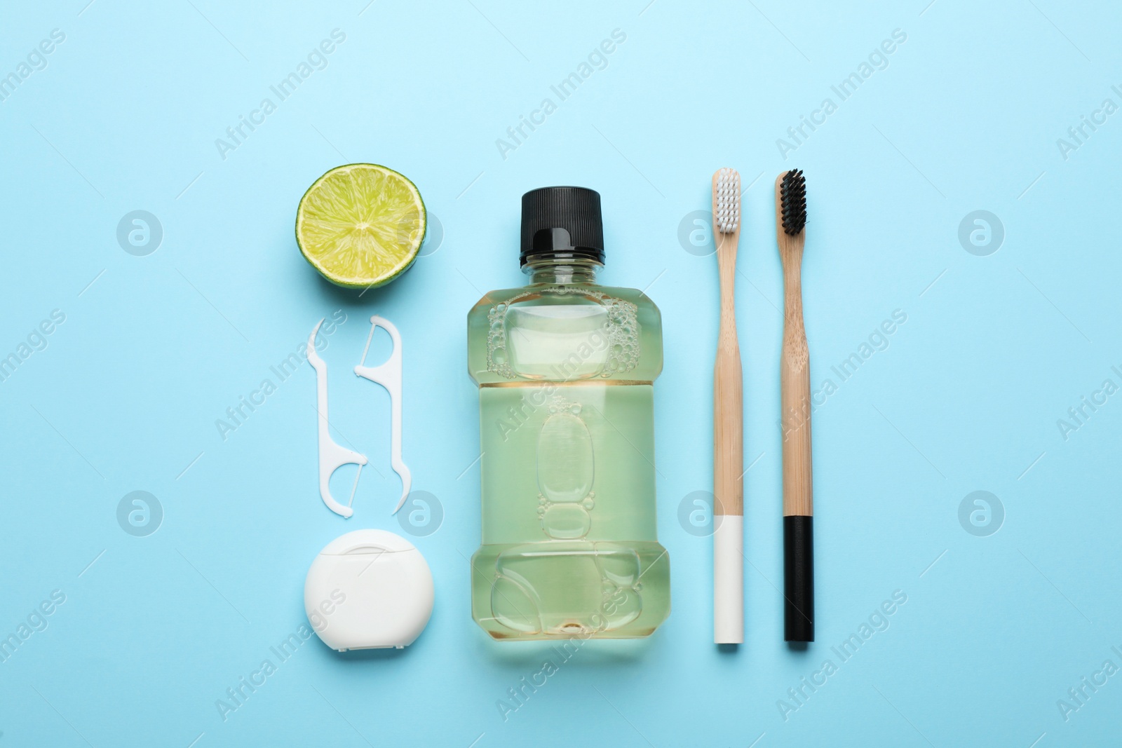 Photo of Mouthwash, toothbrushes, dental floss and lime on light blue background, flat lay