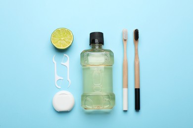 Photo of Mouthwash, toothbrushes, dental floss and lime on light blue background, flat lay