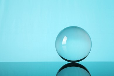 Photo of Transparent glass ball on mirror surface against turquoise background. Space for text