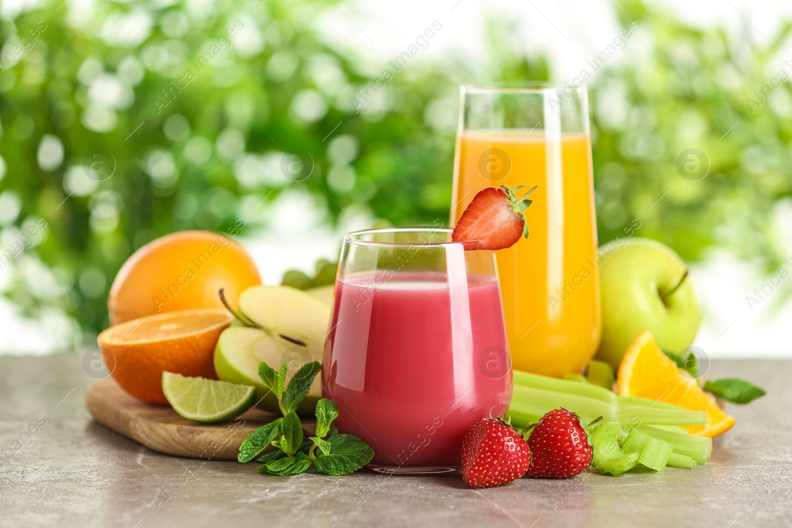 Photo of Glasses with different juices and fresh fruits on table against blurred background