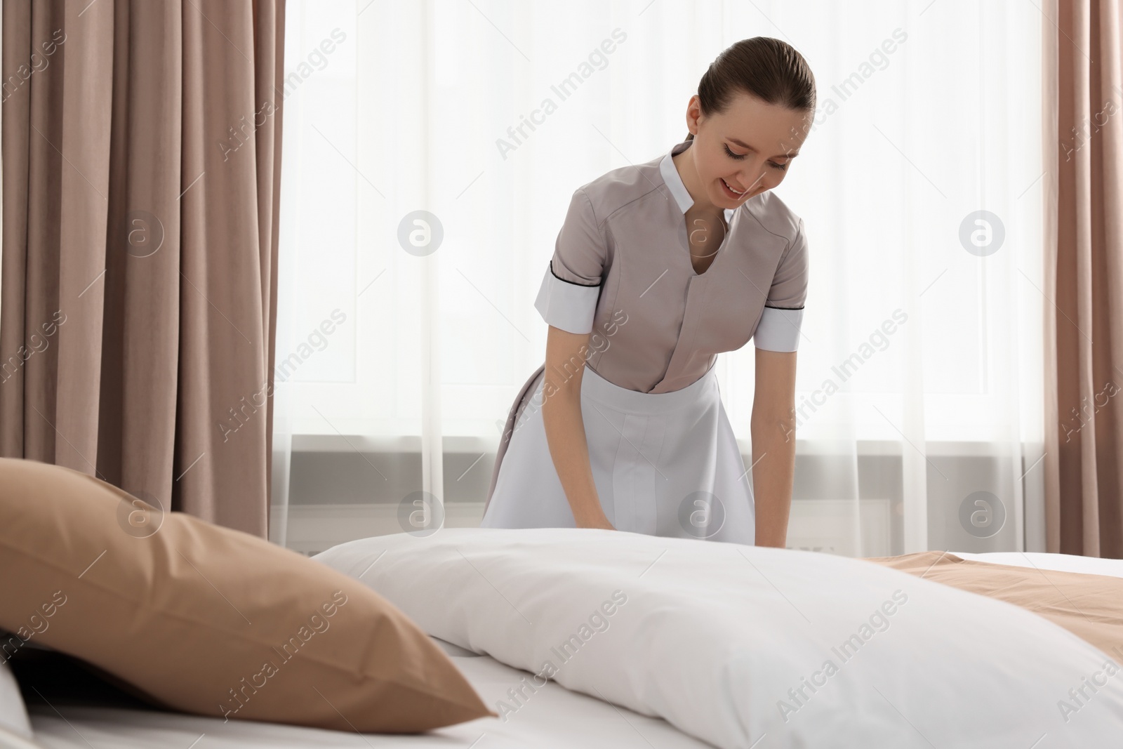 Photo of Young maid making bed in hotel room