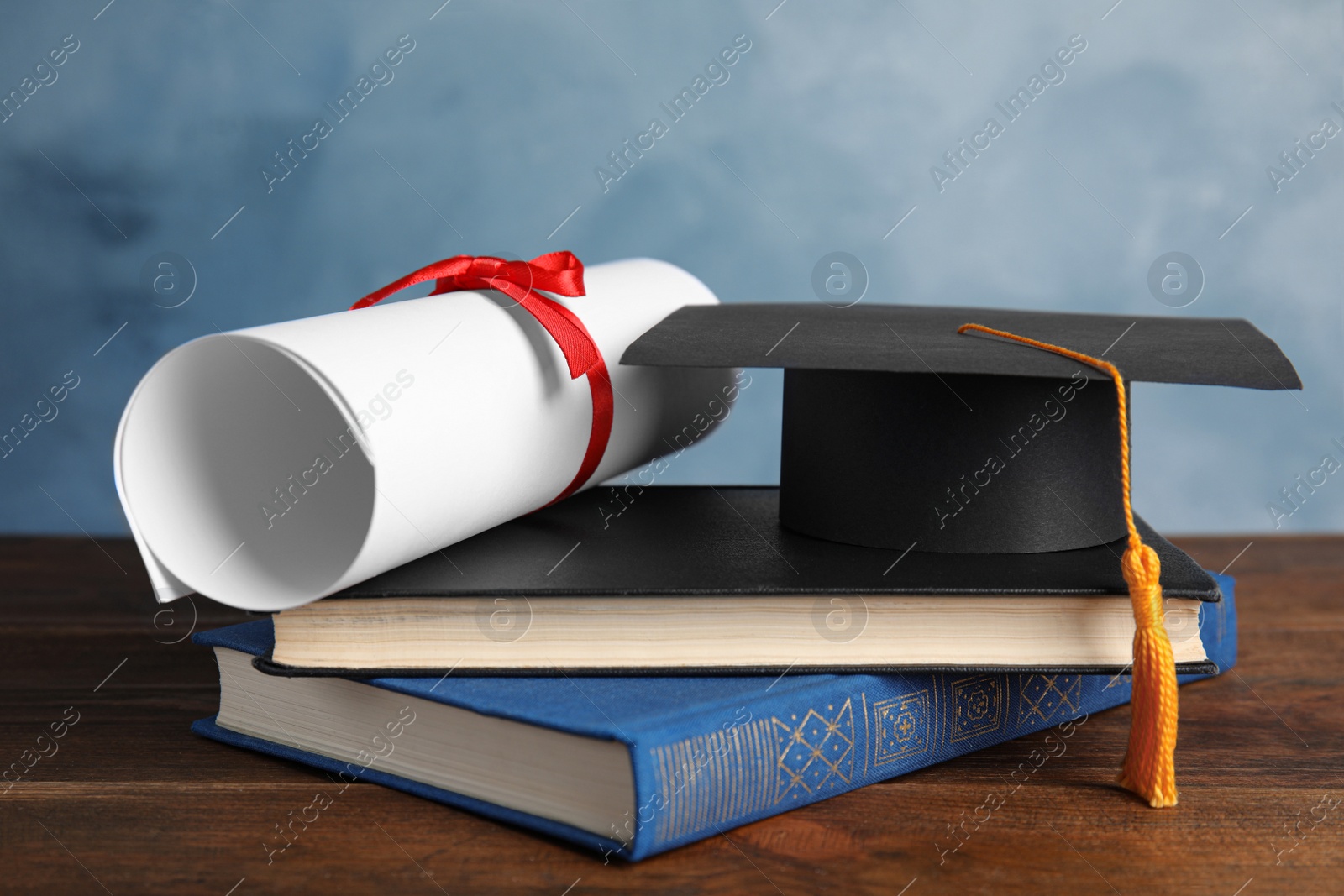 Photo of Graduation hat, books and student's diploma on wooden table against light blue background