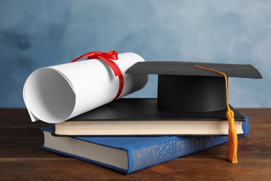 Graduation hat, books and student's diploma on wooden table against light blue background