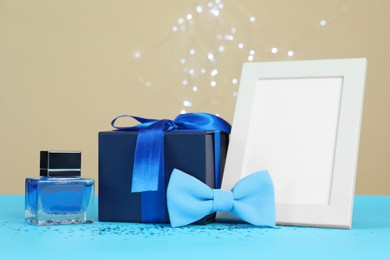 Photo of Happy Father's Day. Empty frame, bow tie, perfume and gift box on light blue table, closeup. Space for text