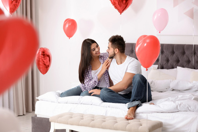 Photo of Lovely young couple in bedroom decorated with heart shaped balloons. Valentine's day celebration