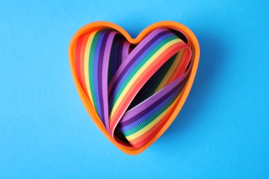 Heart shaped mold with bright rainbow ribbon on color background, top view. Symbol of gay community