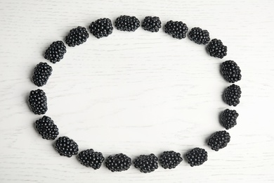 Photo of Frame made of tasty blackberries on white wooden table, top view with space for text