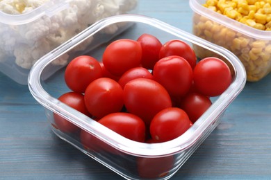 Photo of Glass container with fresh cherry tomatoes on light blue wooden table, closeup