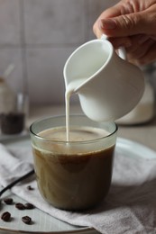 Photo of Woman pouring milk into cup with coffee at table, closeup