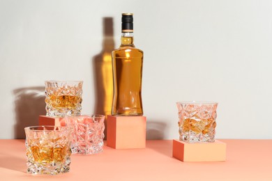 Photo of Stylish presentation of whiskey with ice cubes in glasses and bottle on color background