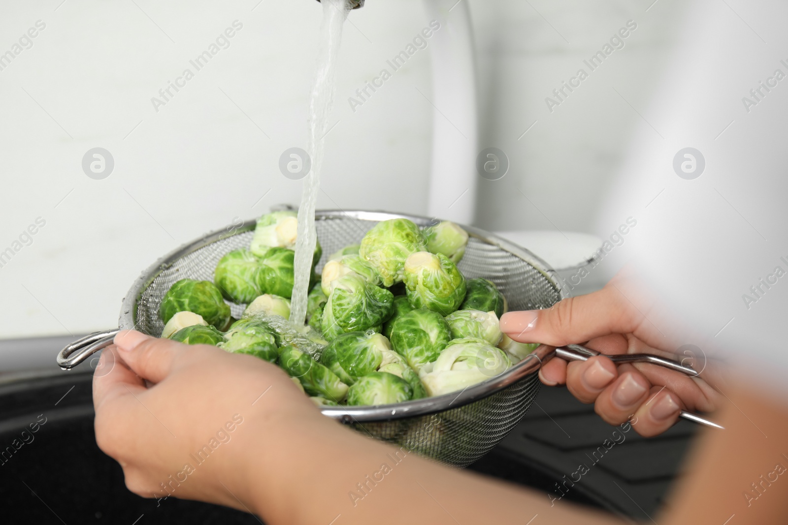 Photo of Woman washing Brussels sprouts with running water over sink, closeup