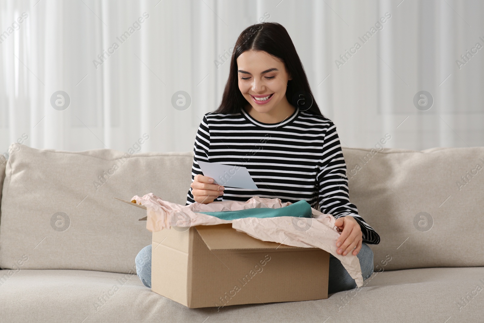 Photo of Happy woman holding greeting card near parcel with Christmas gift at home