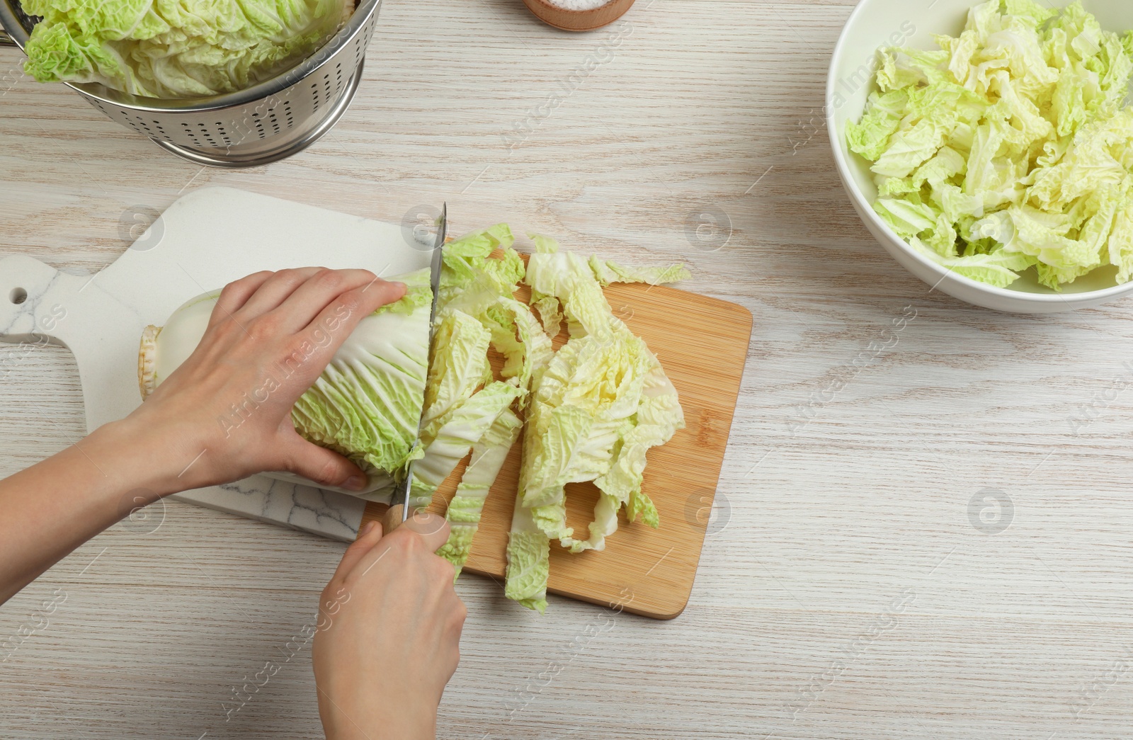 Photo of Woman cutting Chinese cabbage at white wooden kitchen table, closeup