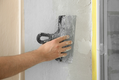 Man plastering window area with putty knife indoors, closeup. Interior repair