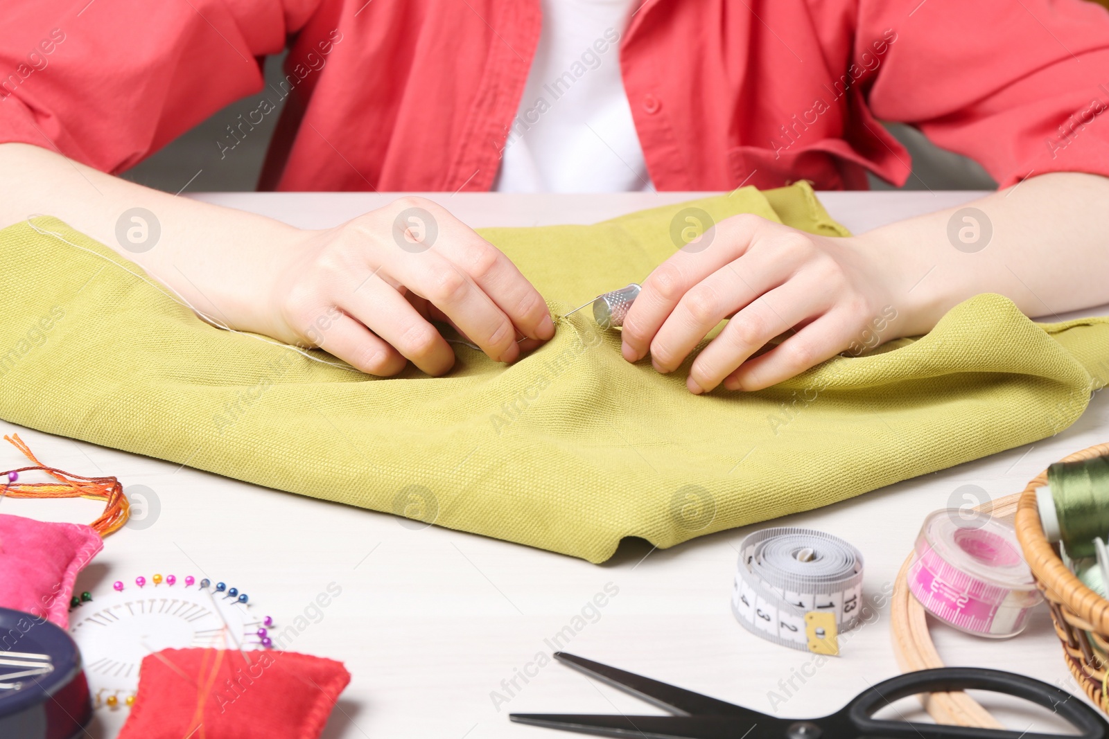 Photo of Woman with sewing needle and thread embroidering on cloth at white table, closeup