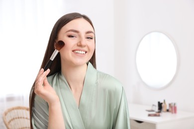 Beautiful young woman applying makeup with brush at home. Space for text