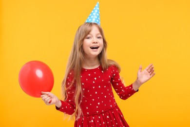 Photo of Happy little girl in party hat with balloon on yellow background