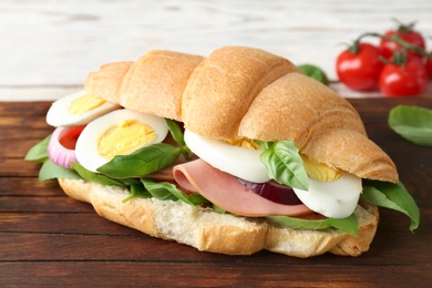 Photo of Tasty croissant sandwich with sausage and eggs on wooden board