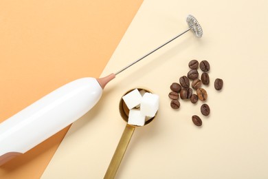 Milk frother wand, coffee beans and sugar cubes on color background, flat lay