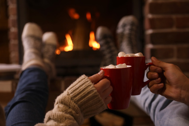 Photo of Couple with cups of delicious cocoa resting near fireplace at home, closeup. Winter vacation