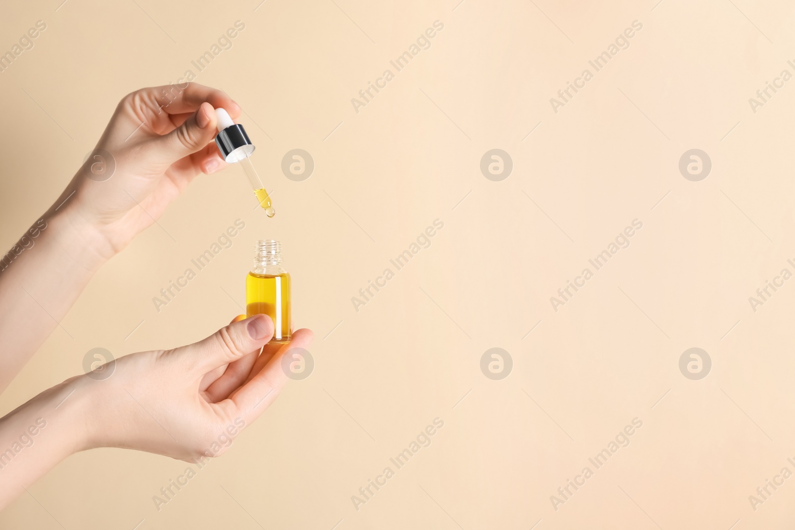 Photo of Woman holding bottle of cosmetic oil on beige background, closeup. Space for text