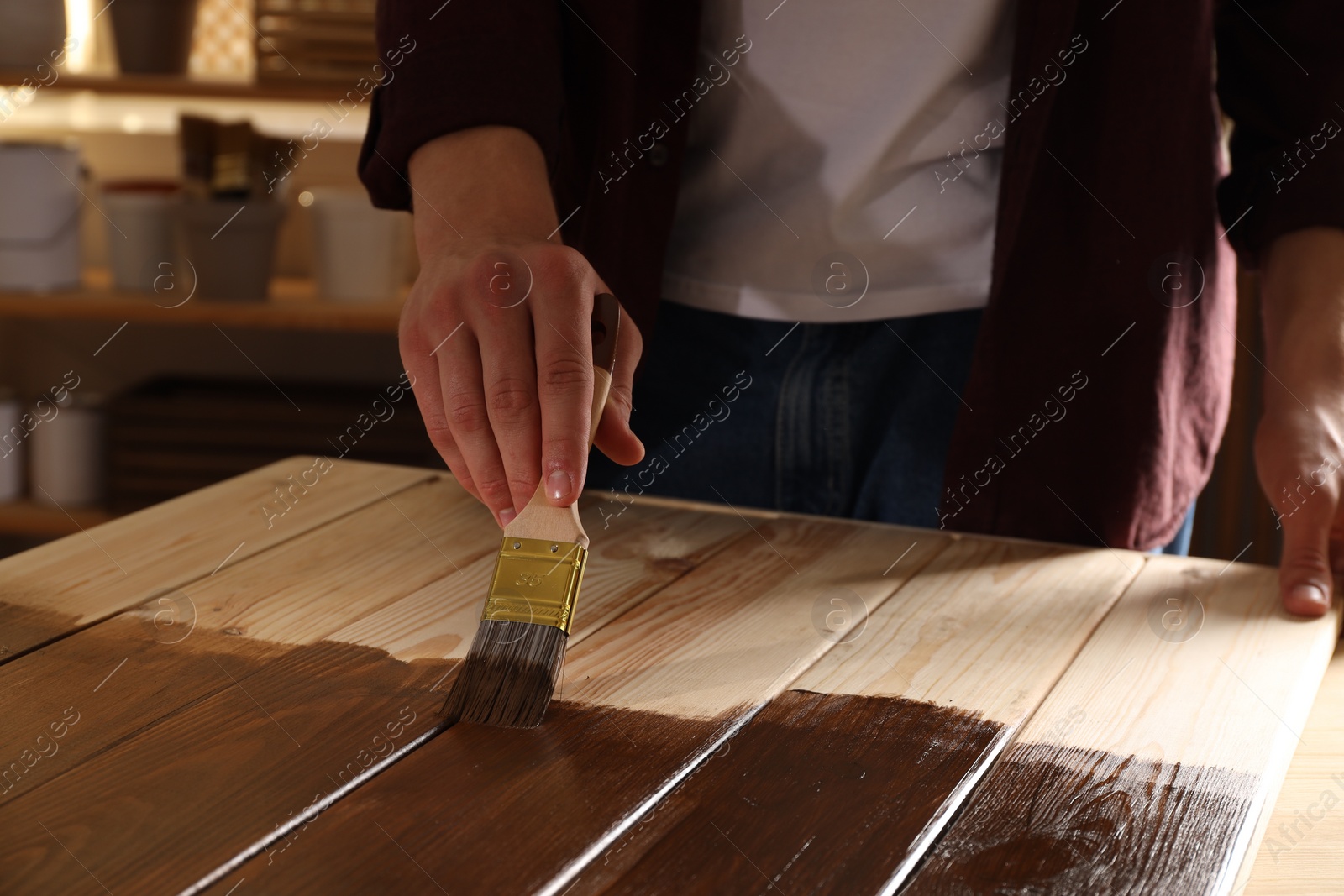 Photo of Man with brush applying wood stain onto wooden surface indoors, closeup