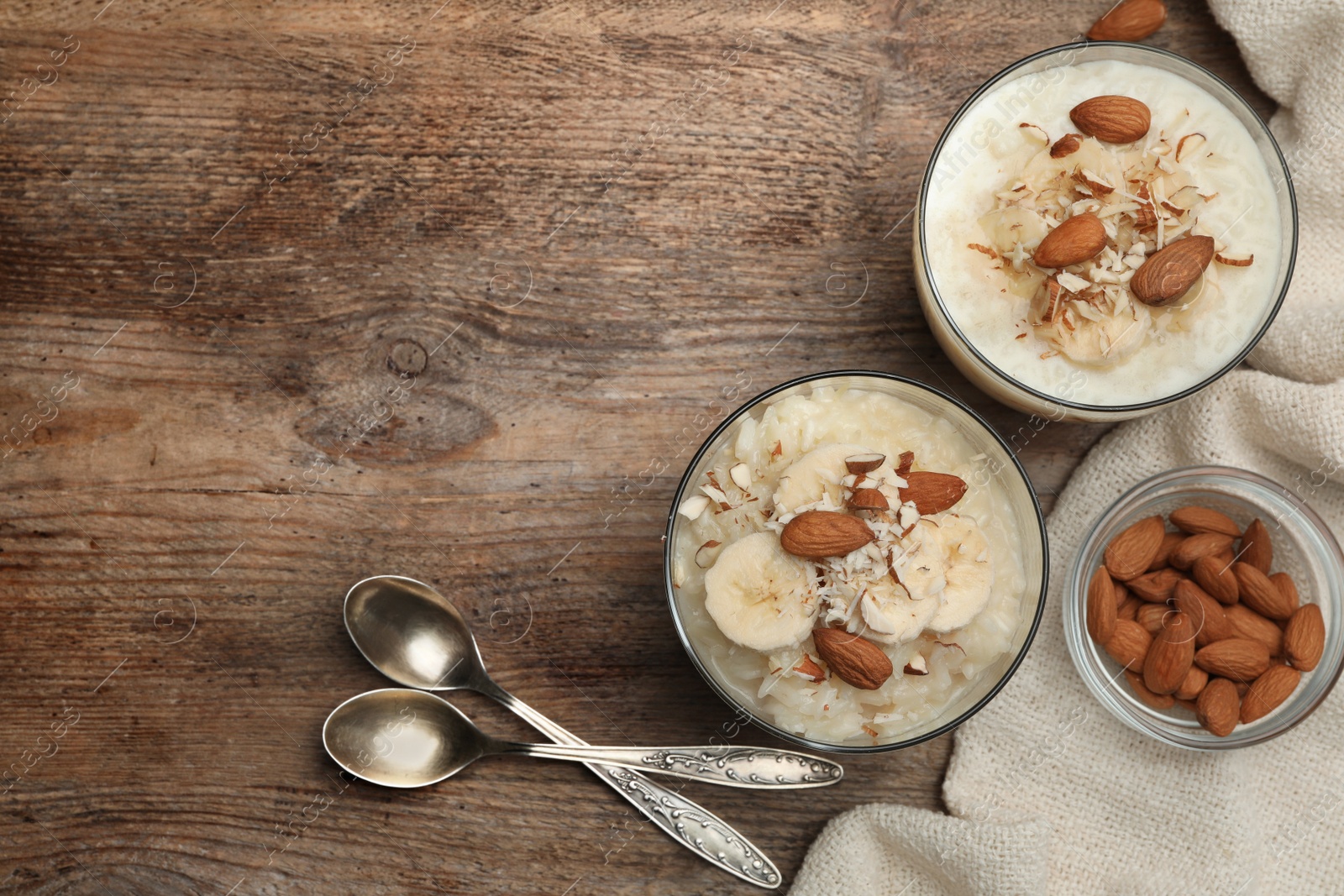 Photo of Delicious rice pudding with banana and almonds on wooden table, flat lay. Space for text