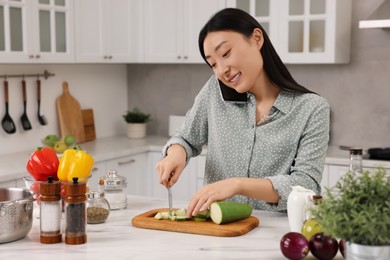 Photo of Smiling woman talking by smartphone while cooking in kitchen