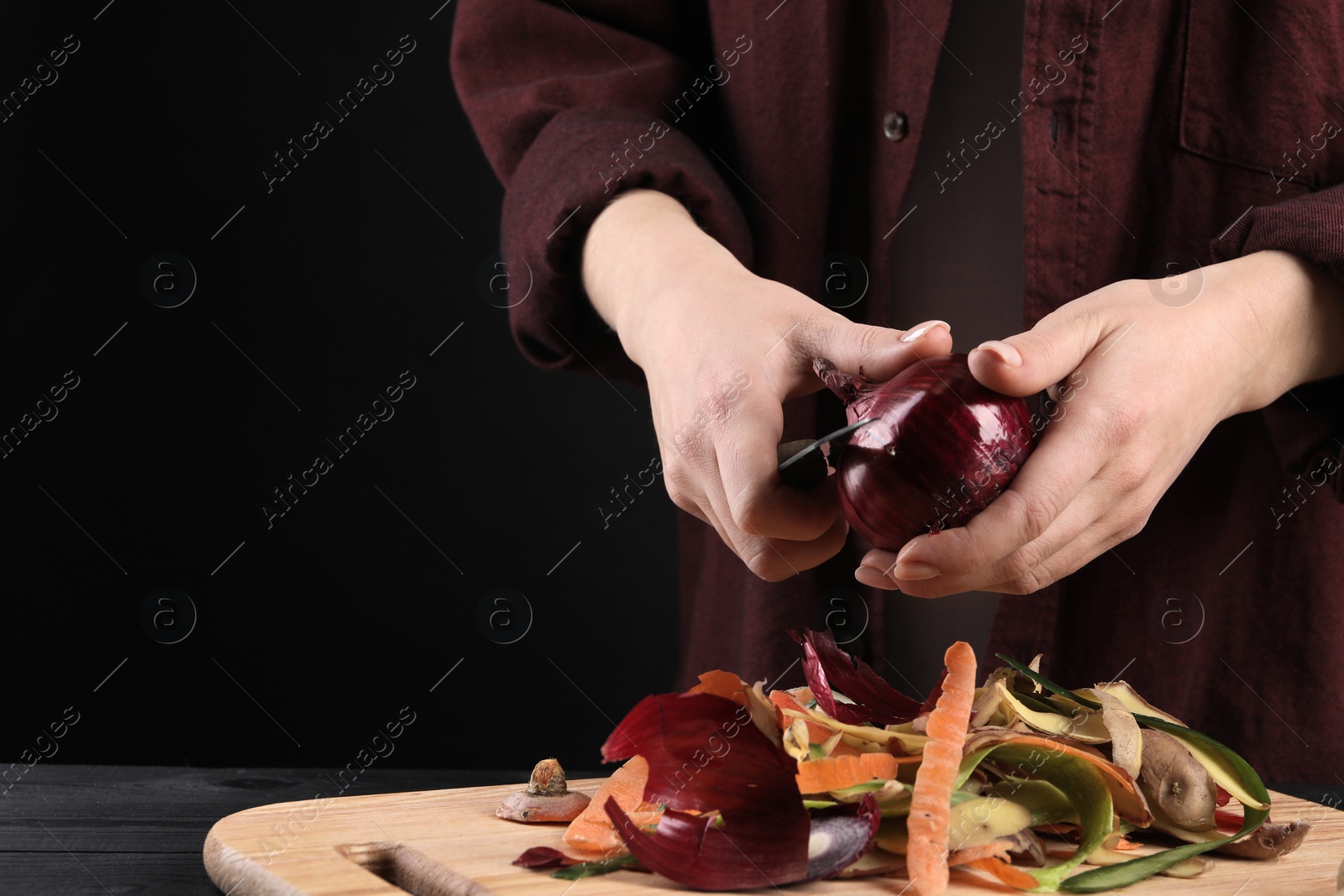 Photo of Woman peeling fresh onion with knife at black wooden table, closeup. Space for text