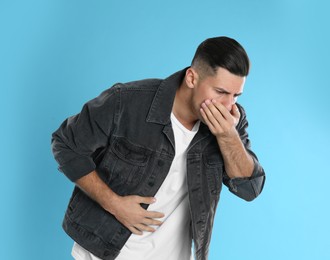 Photo of Man suffering from stomach ache and nausea on light blue background. Food poisoning