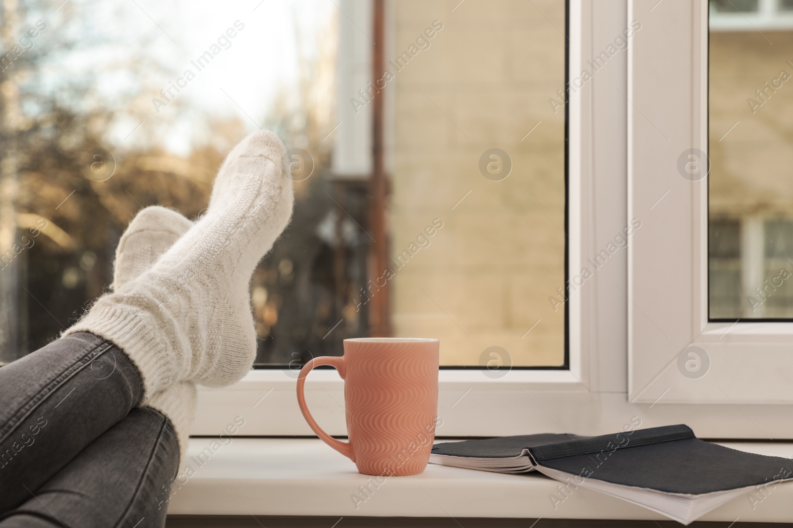 Photo of Woman with cup of winter drink and notebook near window, closeup. Space for text