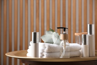 Photo of Bottle with dispenser cap, cosmetic products and towels on tray indoors